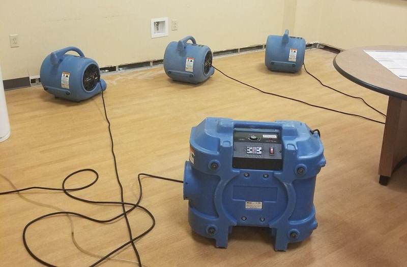 Blue air movers and dehumidifier drying a room with removed baseboards after water damage