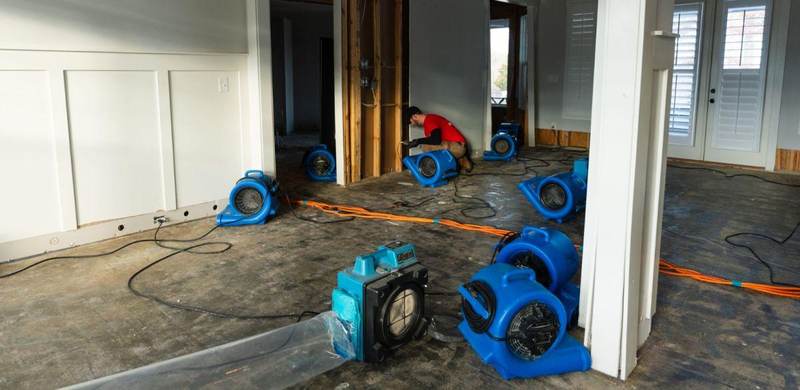 Technician positioning air movers and drying equipment in a water-damaged Texas home