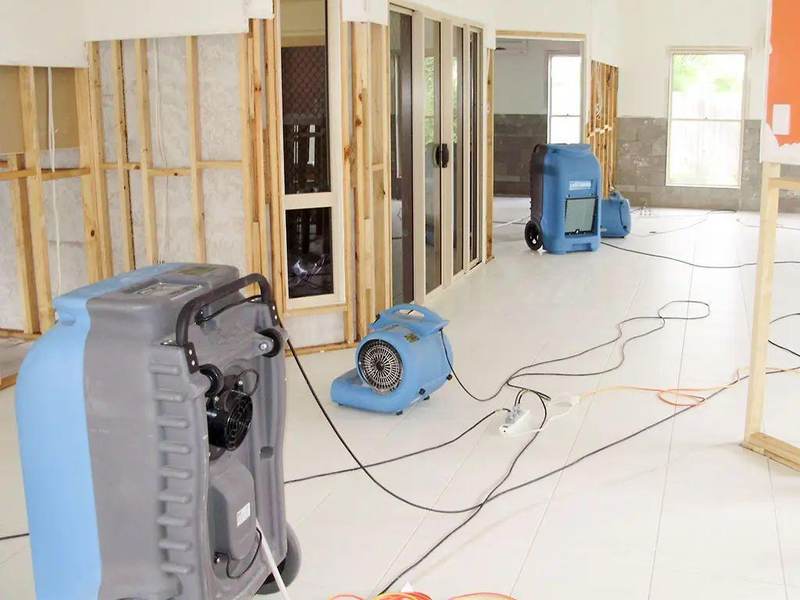 Air movers and dehumidifiers drying a gutted Texas room with exposed wall framing