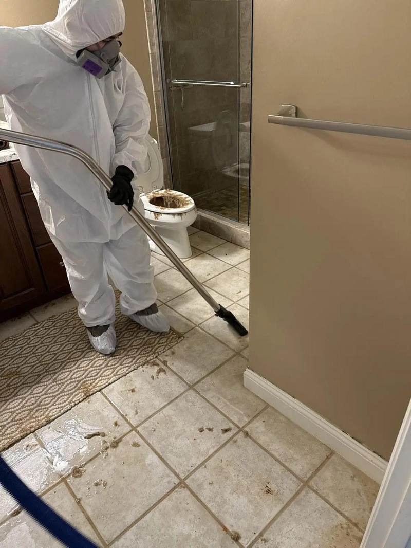 Technician in full protective suit cleaning a sewage backup around a Texas toilet